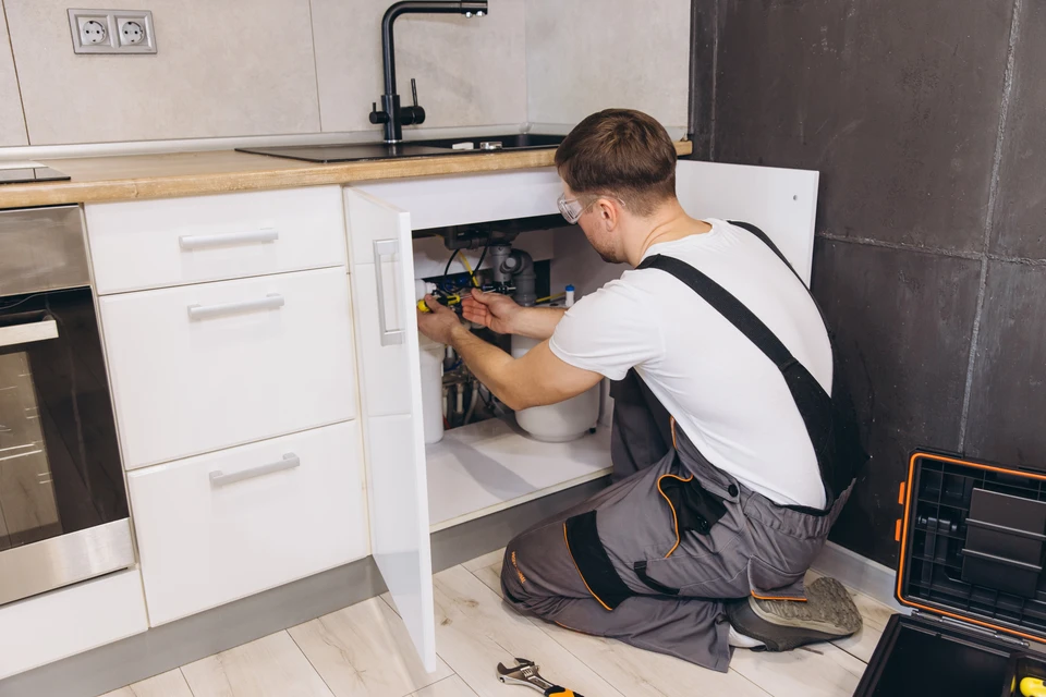 plombier Professionnel portant des lunettes de sécurité travaillant sous l'évier de la cuisine à l'aide d'outils et réparant les tuyaux et l'équipement