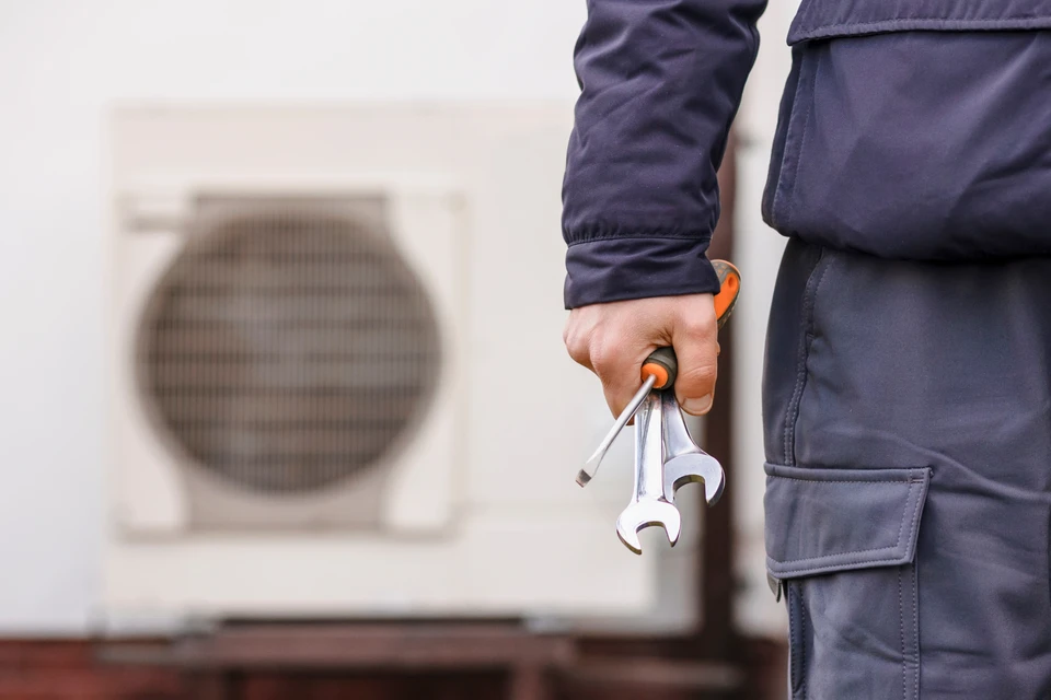 Technicien en combinaison bleue saluant depuis la portière ouverte d'un véhicule utilitaire blanc, tenant un rouleau de câble électrique ou de tuyauterie flexible