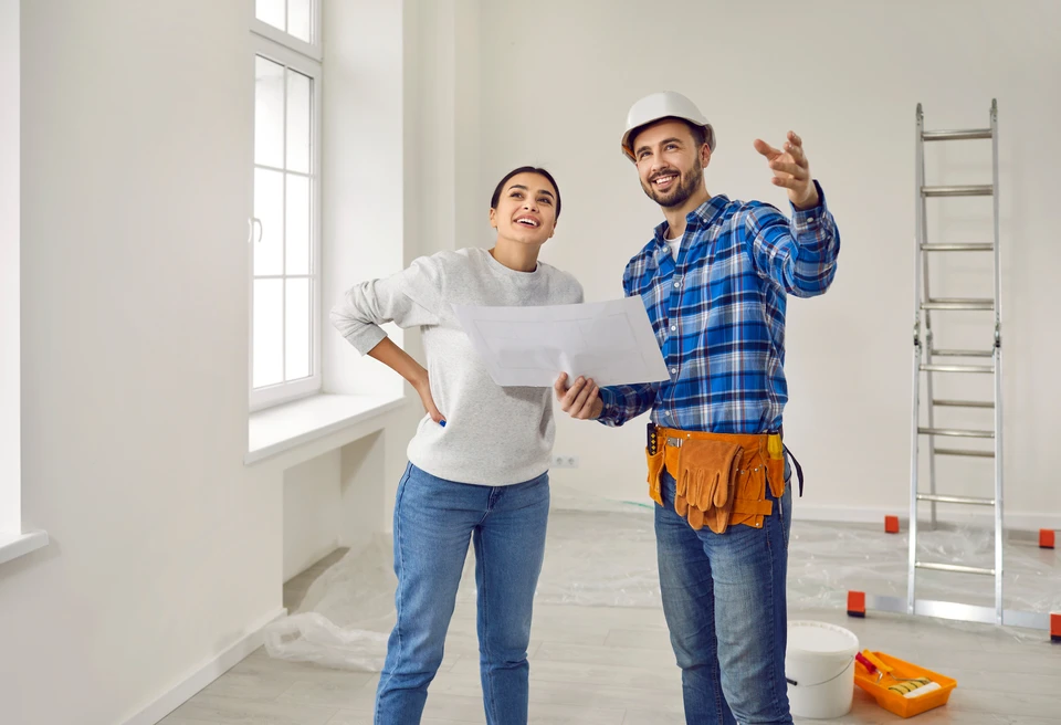 Artisan à genoux installant du parquet dans une pièce blanche, mesurant une lame avec un mètre ruban